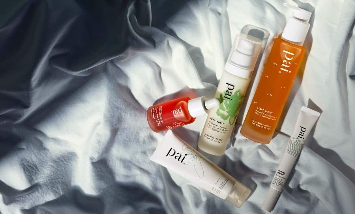 Pai Skincare Bonne Nuit night cream with rosehip oil and cleansers arranged on white linen bedding