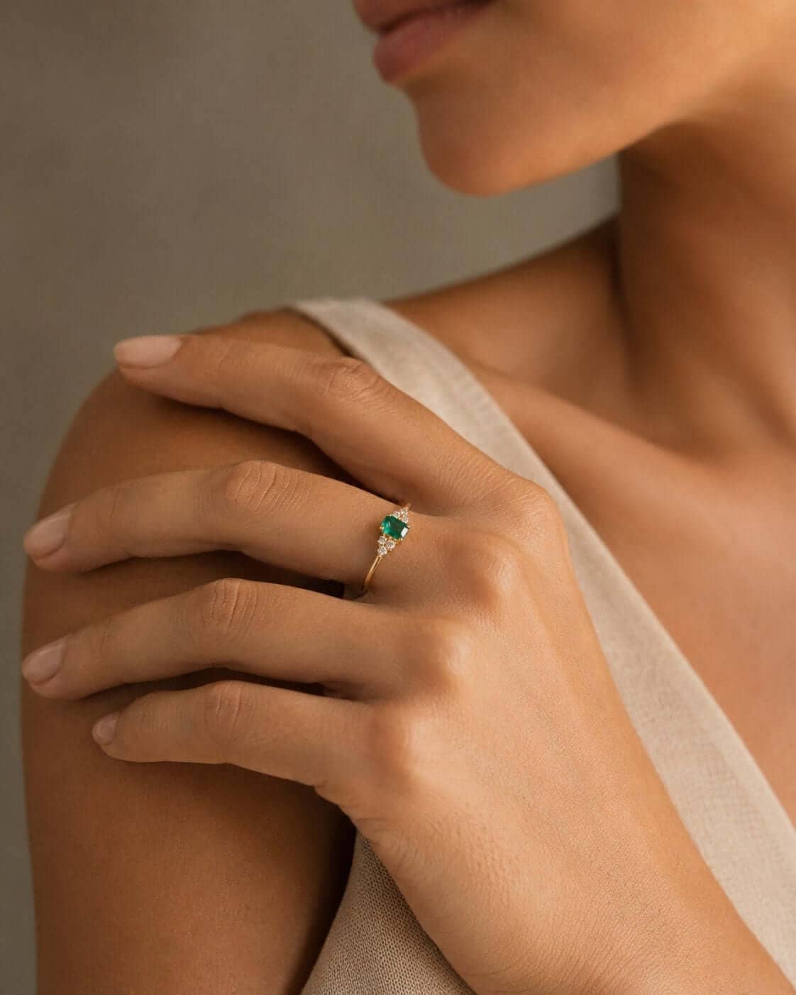 Close-up of a woman’s hand wearing an emerald and diamond ring in yellow gold