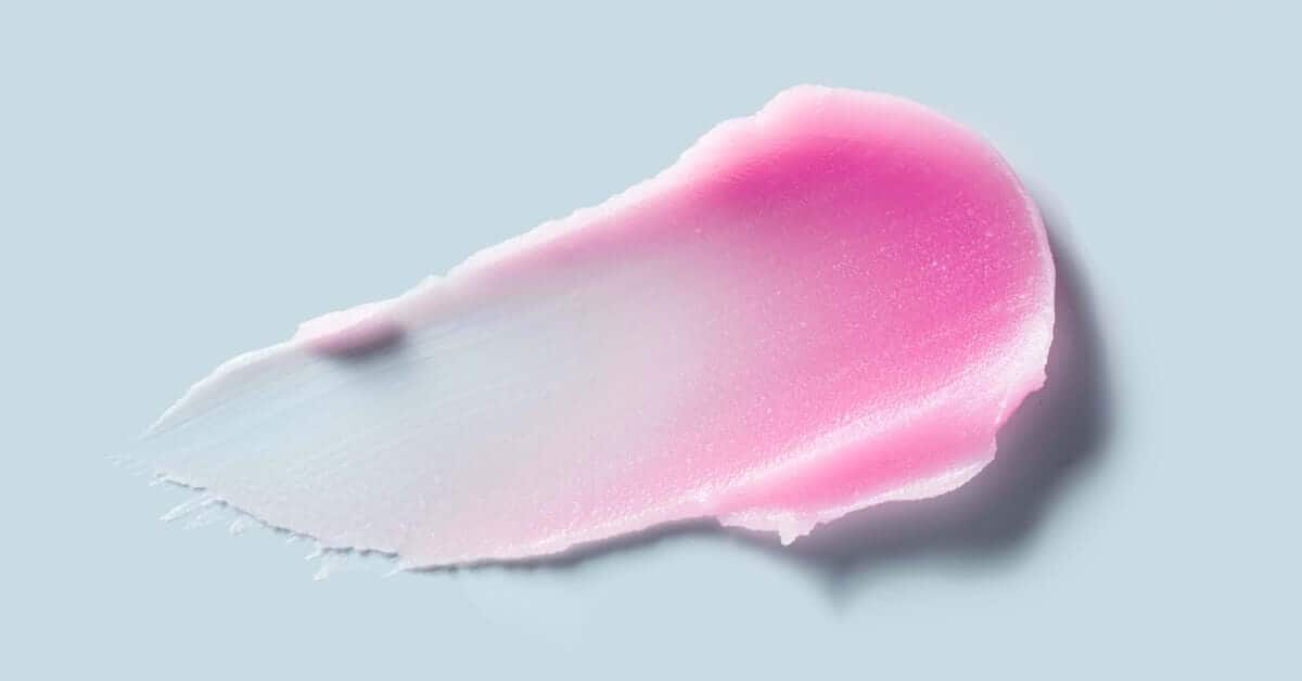 A pink cream wax smear on a light blue background, showing a smooth texture ideal for hair removal or skincare products.