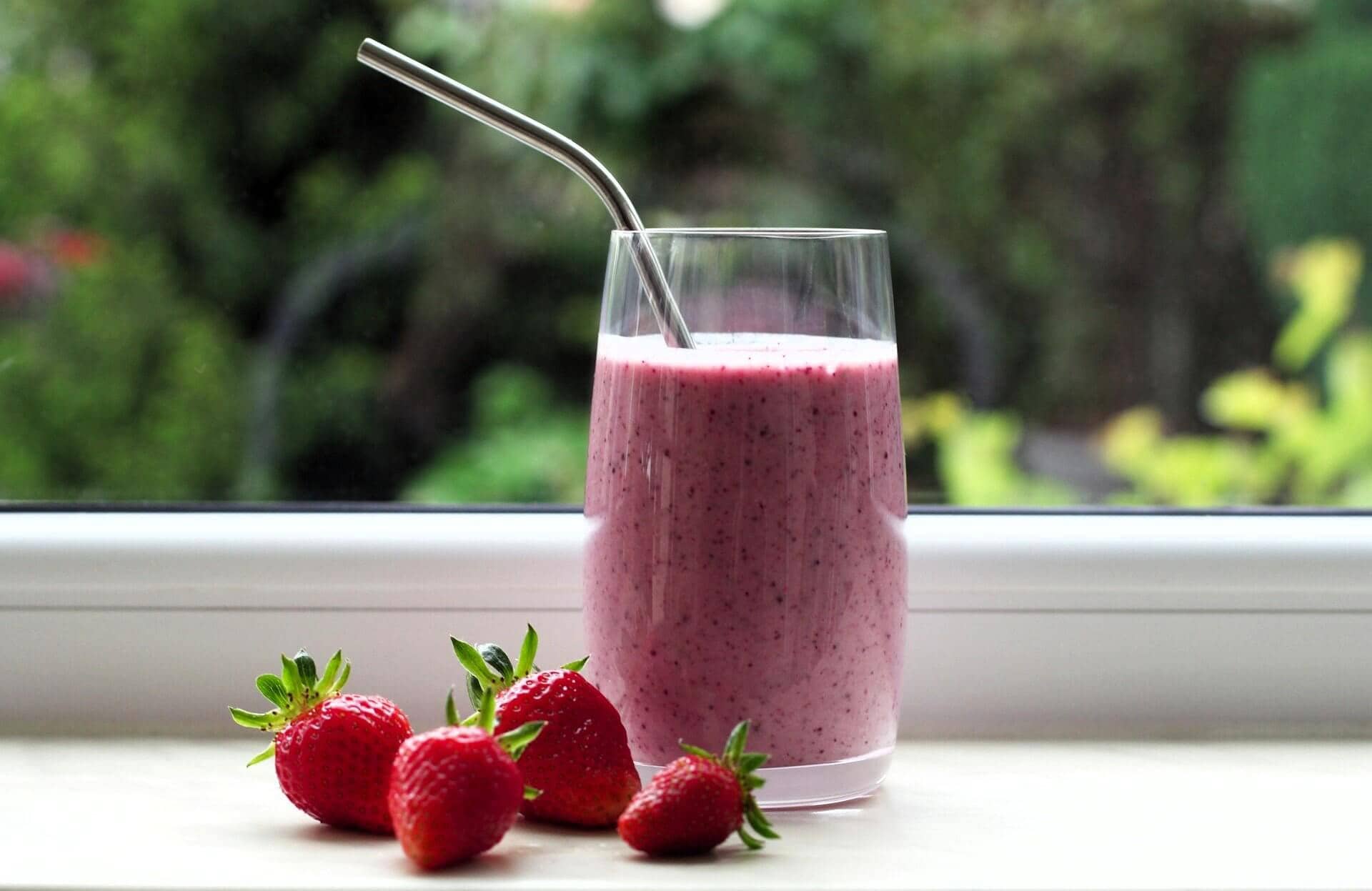 a pink smoothie next to strawberries on a window shelf
