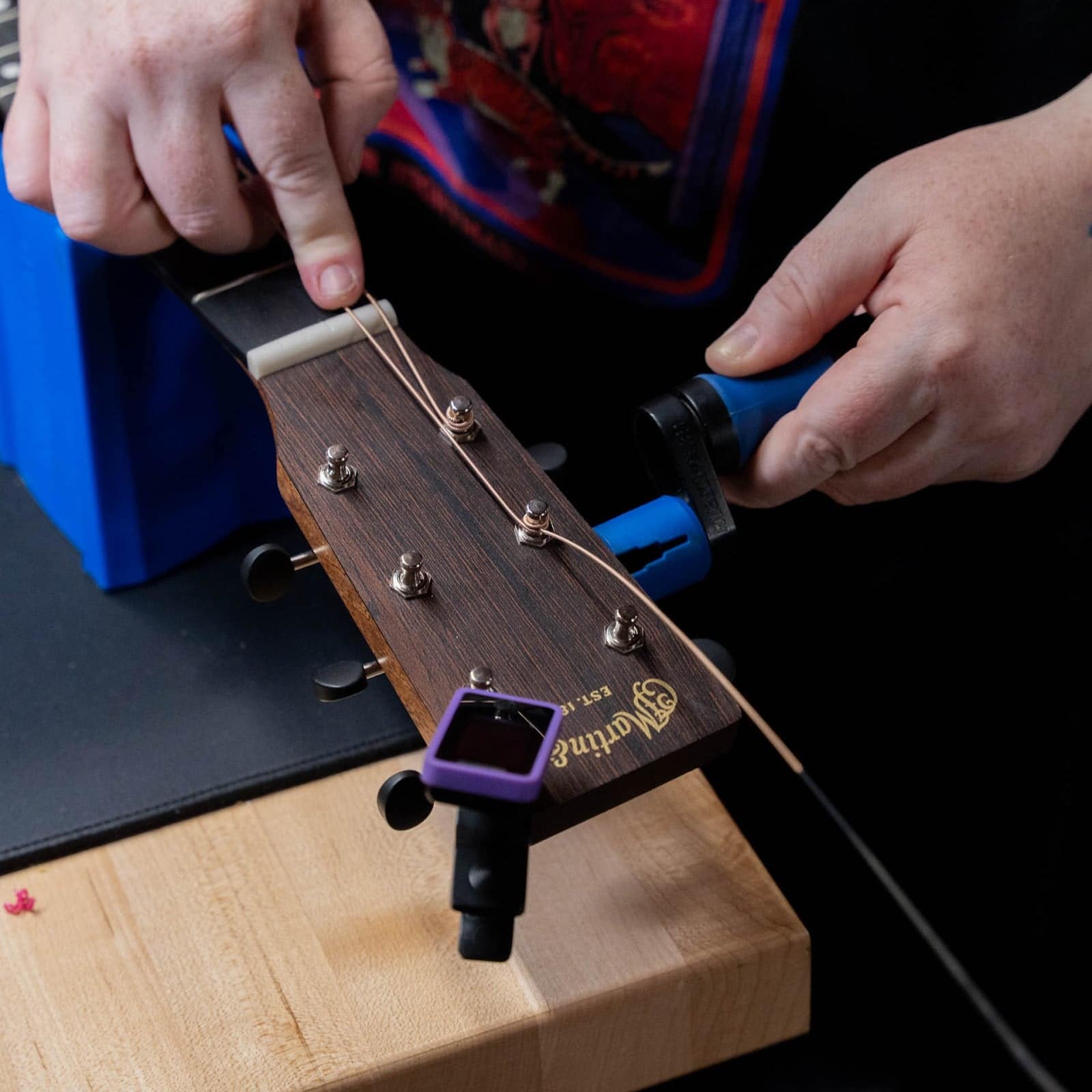 Technician restringing a Martin guitar with a string winder at the TAS bench