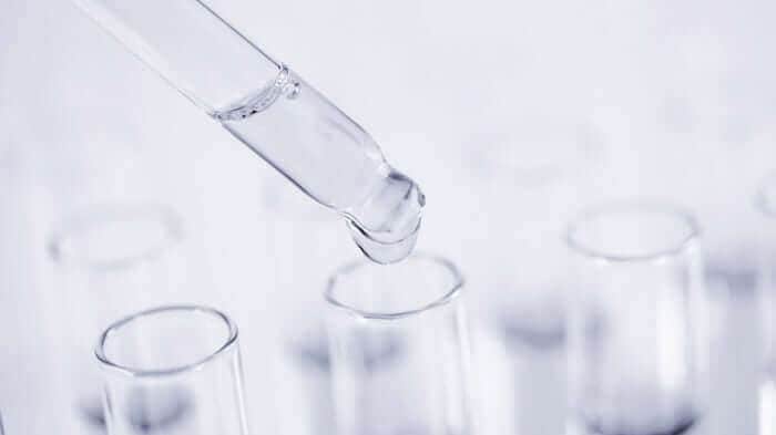 Clear glass dropper dispensing serum into test tubes in laboratory setting for skincare formulation research