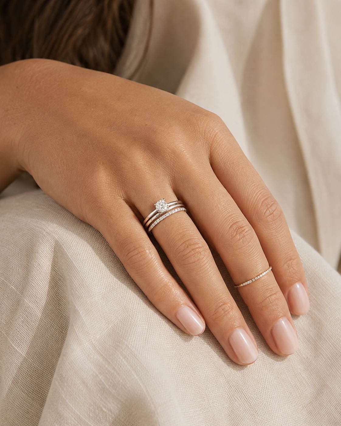 Balanced diamond solitaire, plain band and slim eternity ring stack on a woman's hand