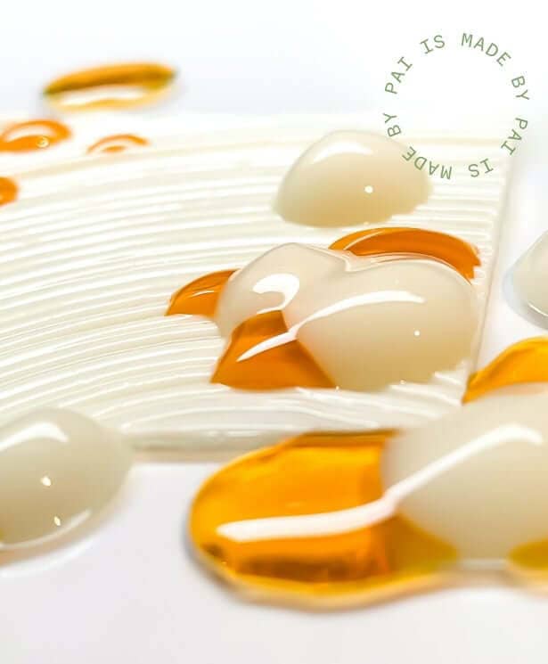 Close-up texture shot showing golden orange oil droplets and clear gel-like serum on white ridged surface