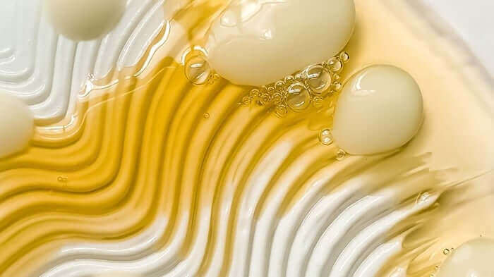 Golden face oil with flowing texture and bubbles showing lightweight serum consistency
