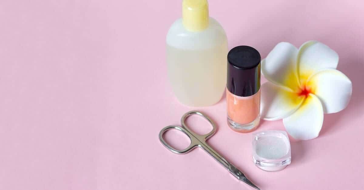 Nail polish, nail remover, scissors used for manicures and pedicures, and a flower are all sitting on a pink background.