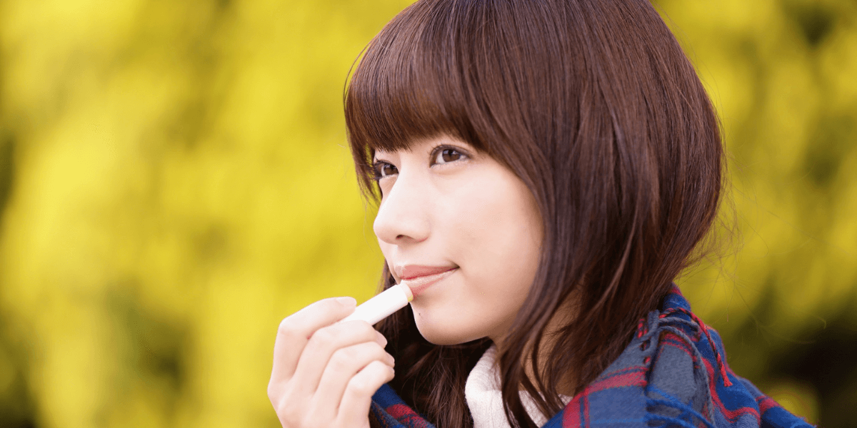 A person applying lip balm outdoors.