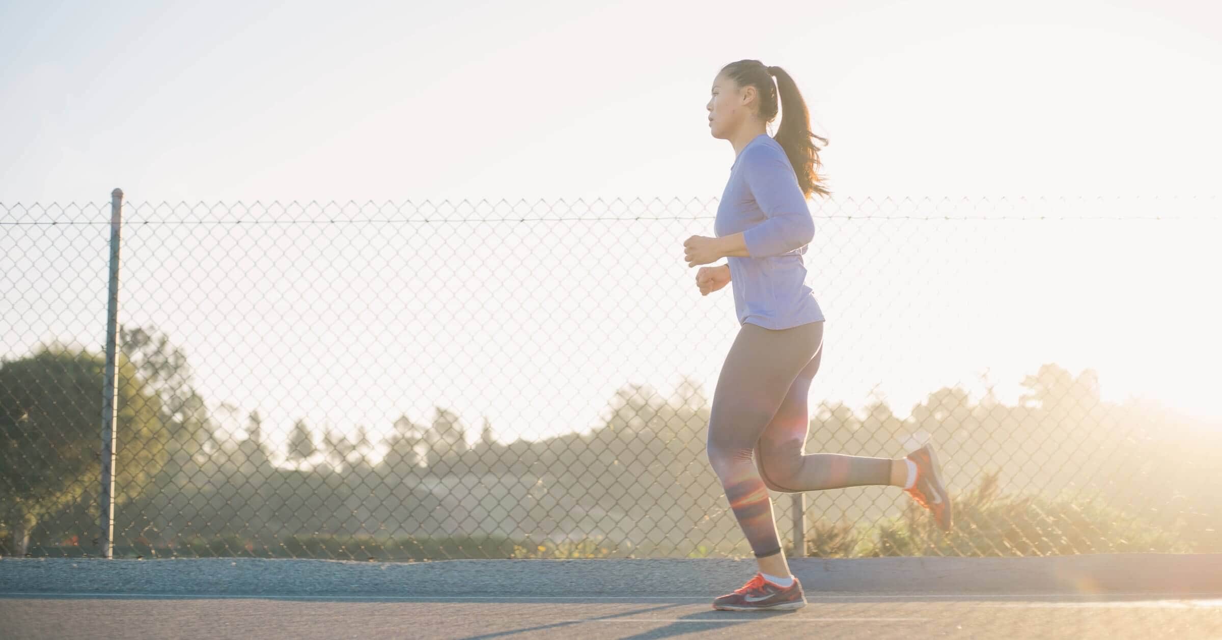 Woman running outdoors in athletic wear at golden hour for skincare and exercise routine