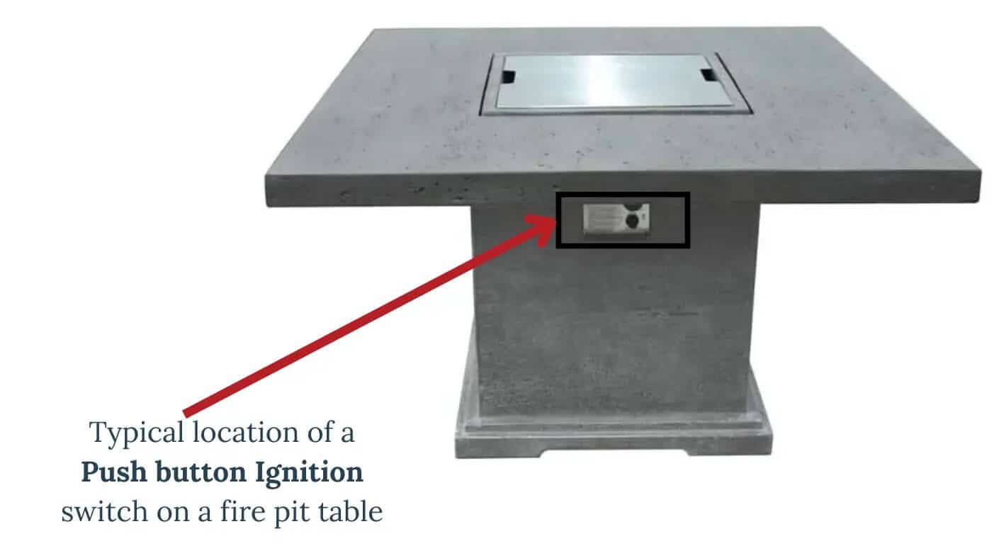 A concrete square fire pit table with a closed burner cover. A red arrow points to a rectangular push-button ignition switch located on the side of the table's base.