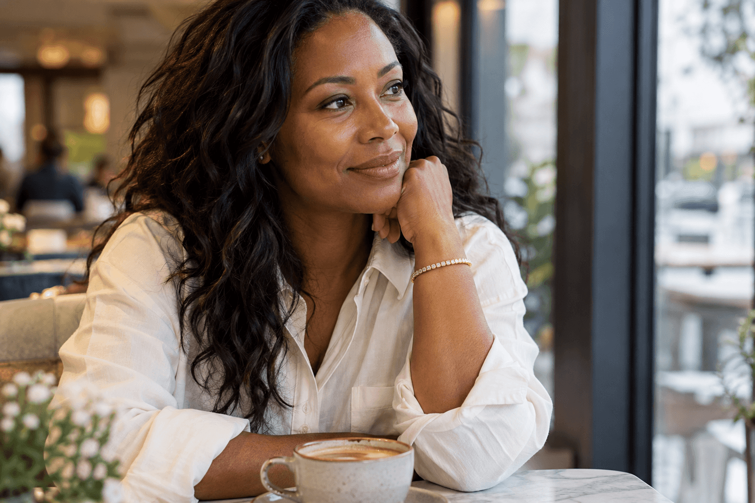 A woman wearing a slender diamond bracelet with a soft shirt cuff at a café table