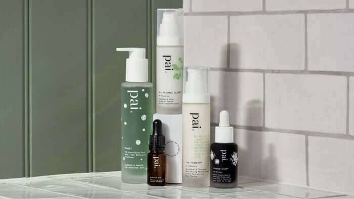 Collection of Pai Skincare acid products including cleanser, serum and treatments displayed on white marble surface against green paneled wall