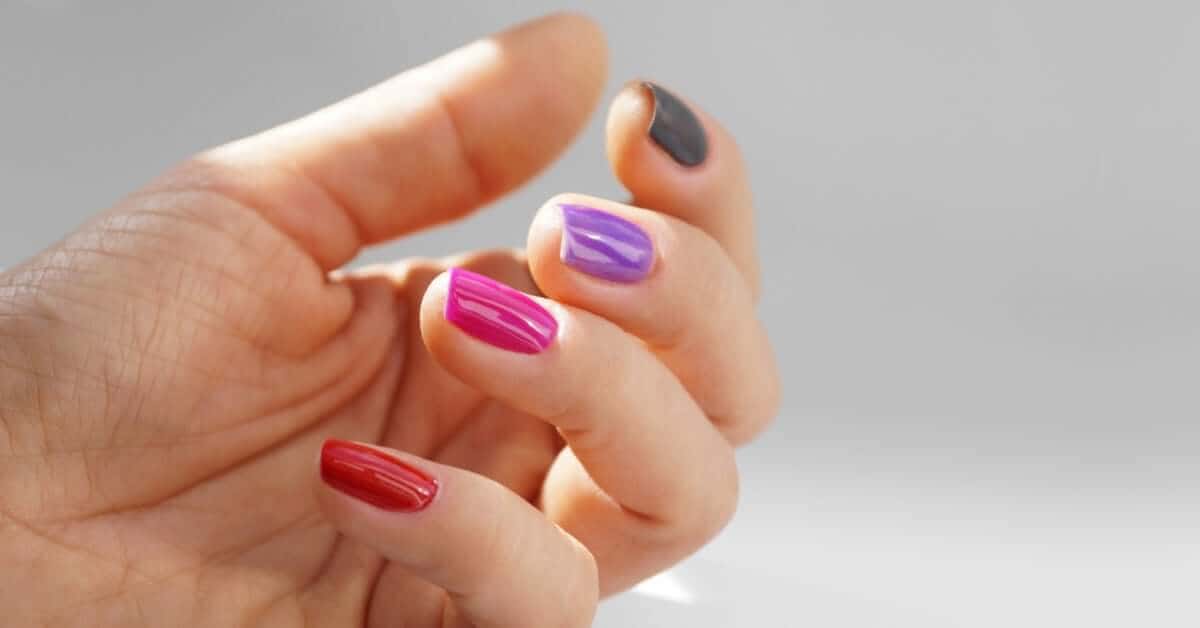 A person displaying their nails. Each nail has a different coat of gel polish, with colors from green to red.