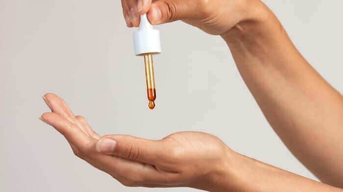 Hand dispensing golden face oil from white dropper bottle onto open palm