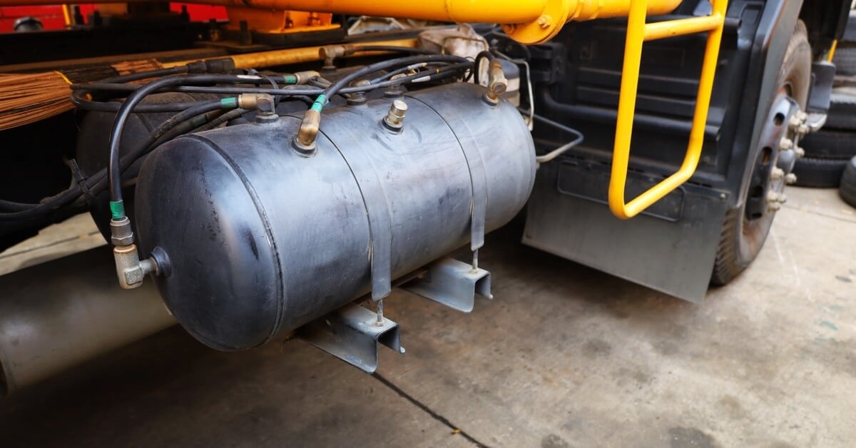 A black cylindrical air tank for a truck's air brake system, with several tubes and brass fittings attached.