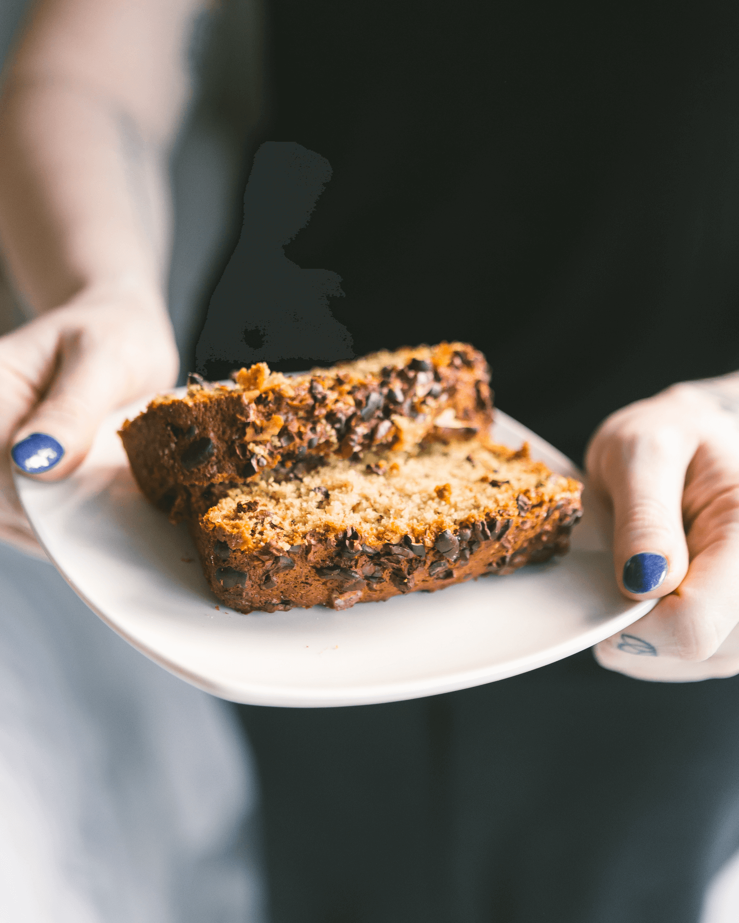 Hands holding a plate with two slices of chocolate chip zucchini bread