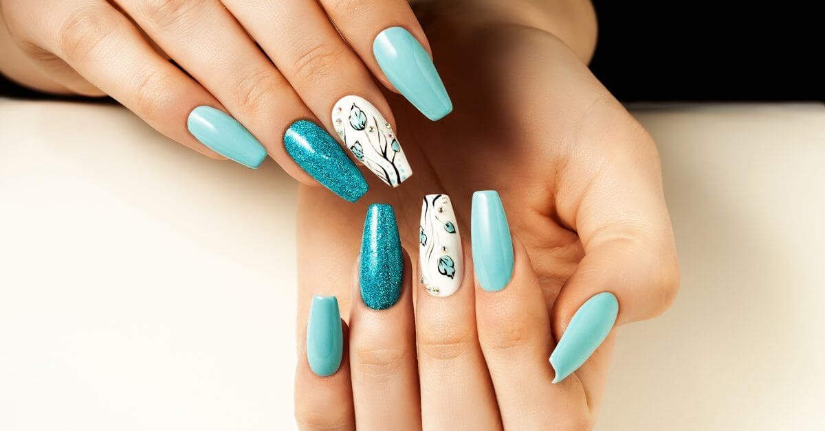 Manicured nails where several nails are light blue, the middle nail has a floral design, and the ring fingernail is glittery.