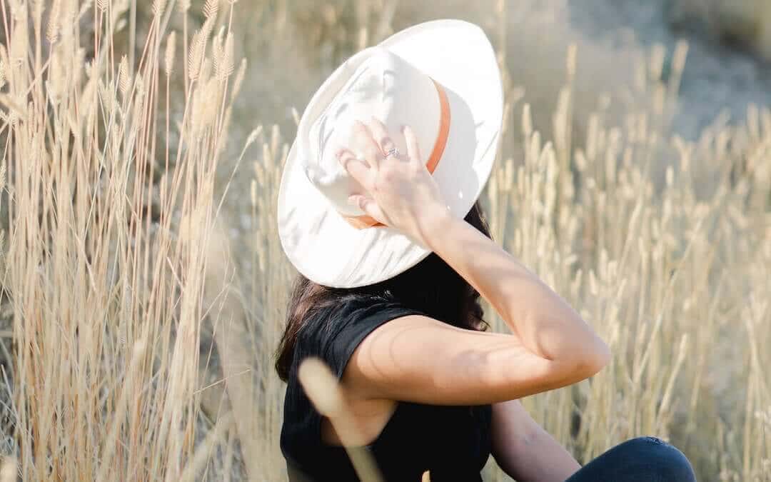 rewire your brain for happiness, woman sitting outdoors, holding hat on head