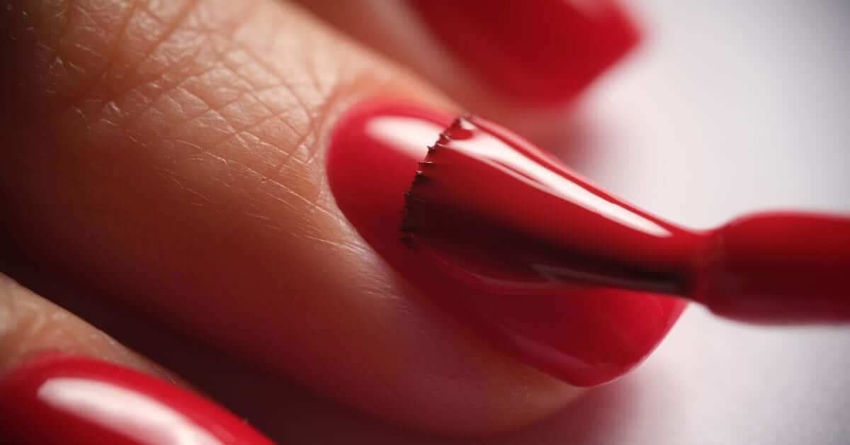 A gel nail polish brush moving over the surface of a person's nail to cleanly apply a bright berry red color.