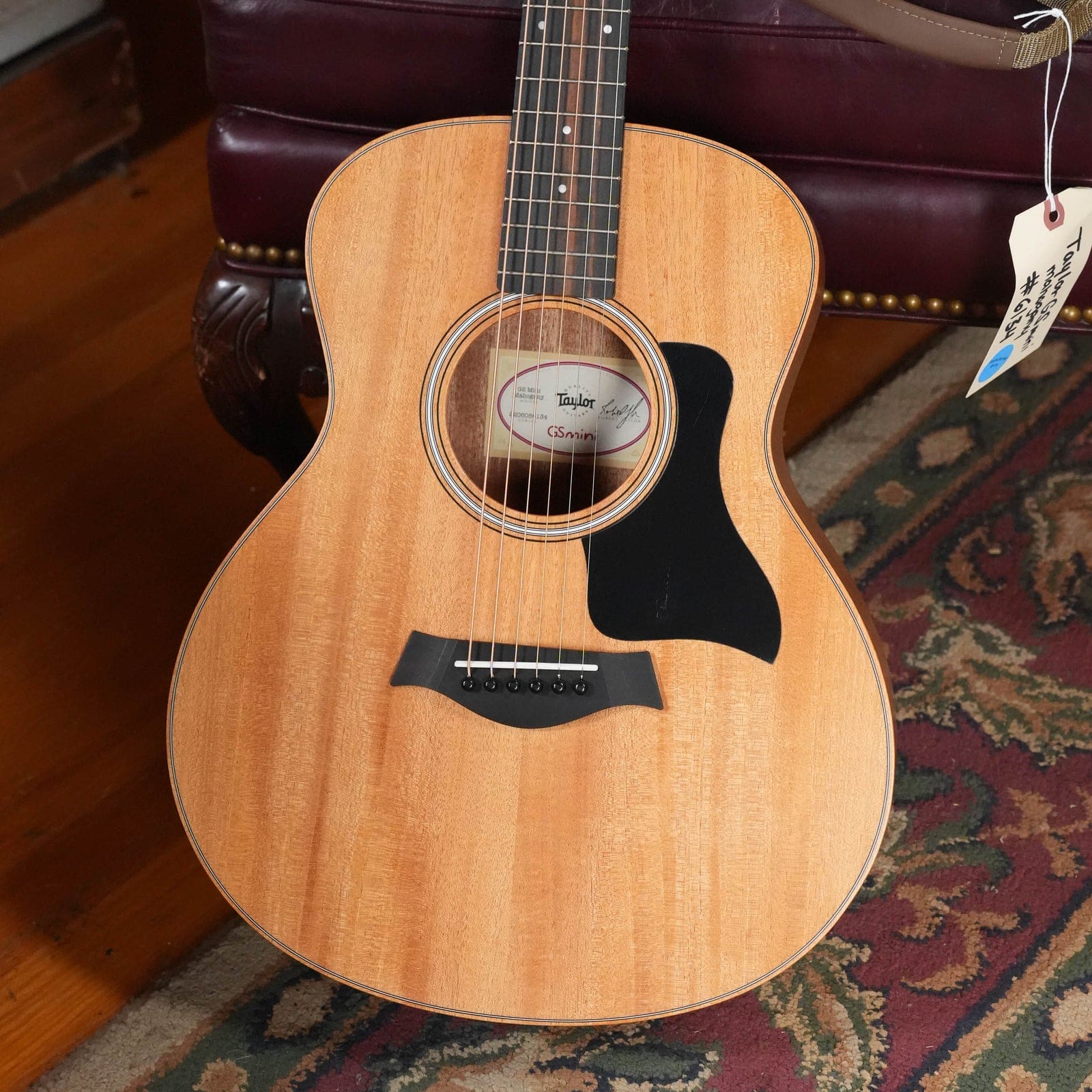 Taylor GS Mini Mahogany with a solid mahogany top and black pickguard, on a rug in our showroom