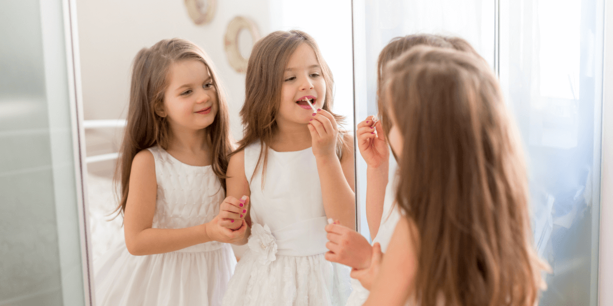 Two children trying lip gloss in front of a mirror.
