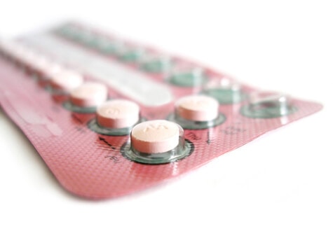 Pink contraceptive pill blister packs showing white tablets in foil packaging