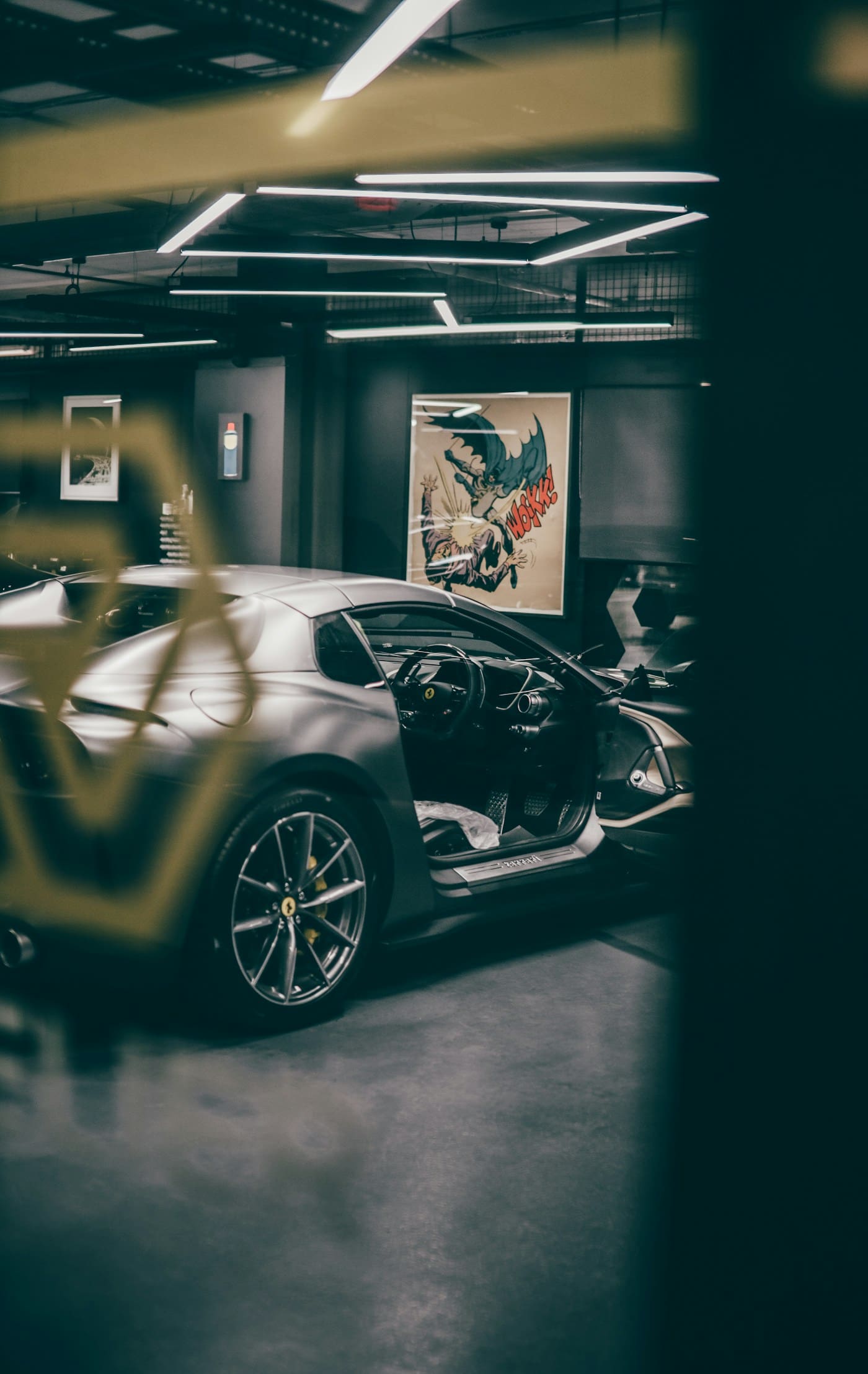 Sports car displayed in a dark garage with framed graphic artwork on the wall
