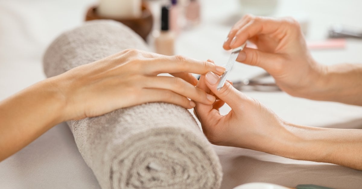 A close-up of a woman doing a manicure in their nail shop. She's filing the customer's nails on top of a towel.