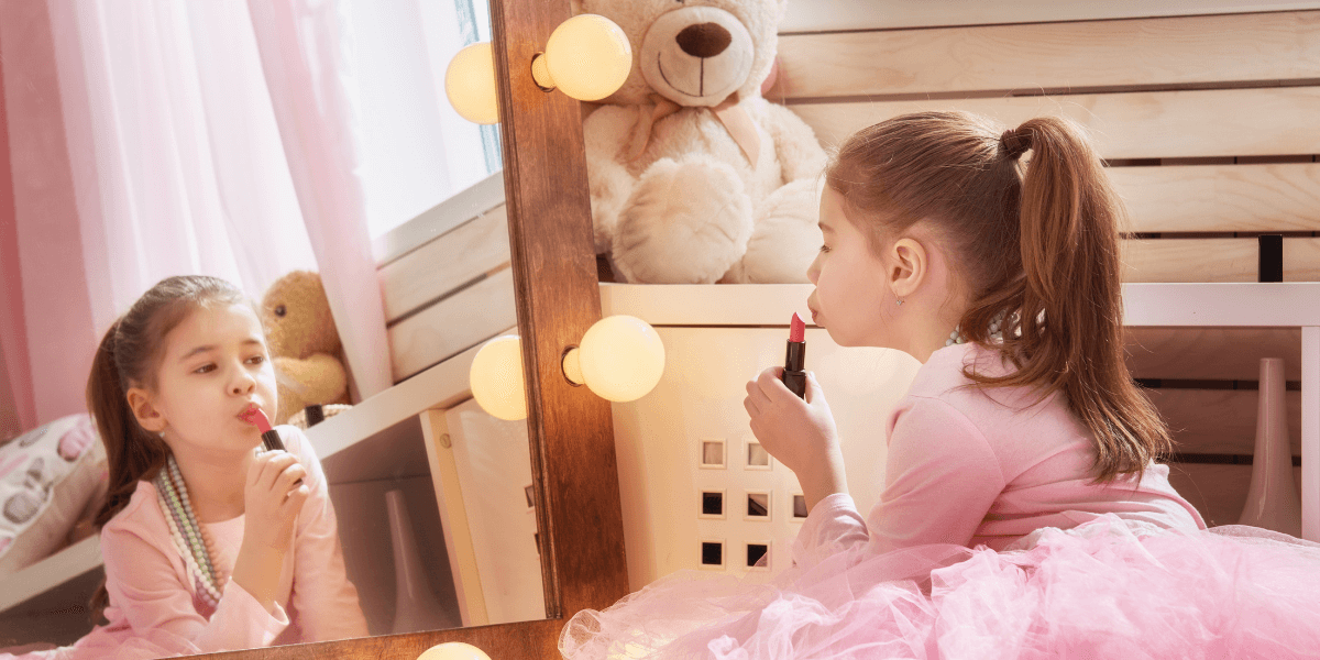 Child applying lipstick while looking in a mirror.