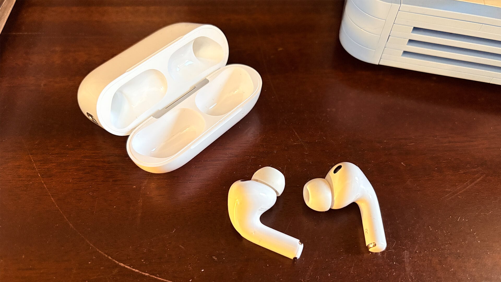 AirPods Pro 3 earbuds resting on a wooden desk with case