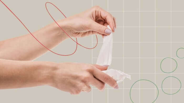 Hands pulling apart a white face wipe against neutral background, demonstrating skincare routine for sensitive skin