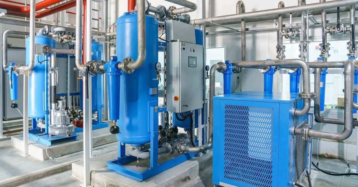 An industrial plant room with blue tanks, silver pipes, red lines, and a central control panel in a clean, bright facility.