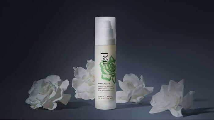 Pai Bonne Nuit Overnight Rebalancing Treatment bottle with white pump dispenser surrounded by delicate white rose petals on dark background