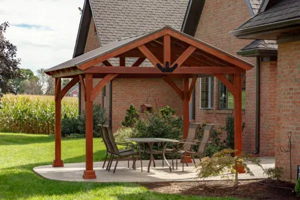 A wooden A-frame pavilion with patio furniture in a backyard.