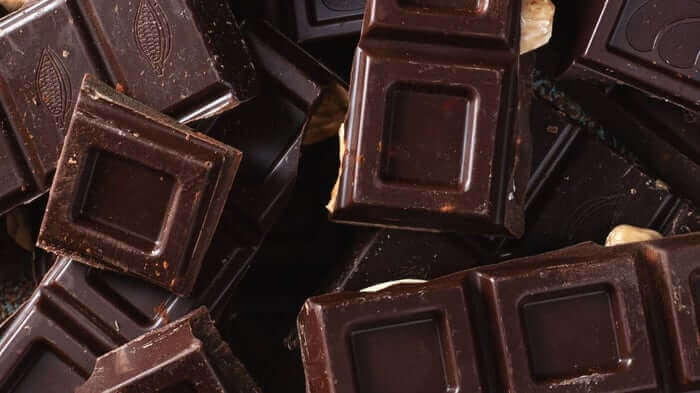 Dark chocolate squares scattered together, showing rich brown texture and glossy surface
