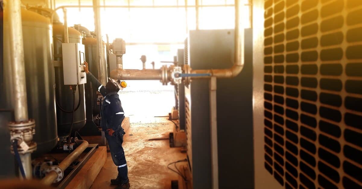 An individual in a blue jumpsuit and white hard hat operating a large air dryer in an industrial setting.