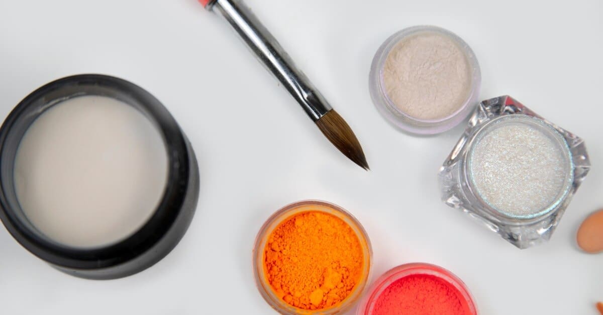An assortment of nail manicure tools, including open jarred powders, coatings, and an acrylic nail brush.
