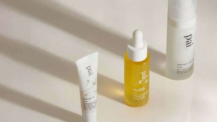 Three Pai Skincare products arranged on white surface with natural shadows - white tube, golden yellow Rosehip BioRegenerate Oil serum, and white spray bottle for sensitive skin care