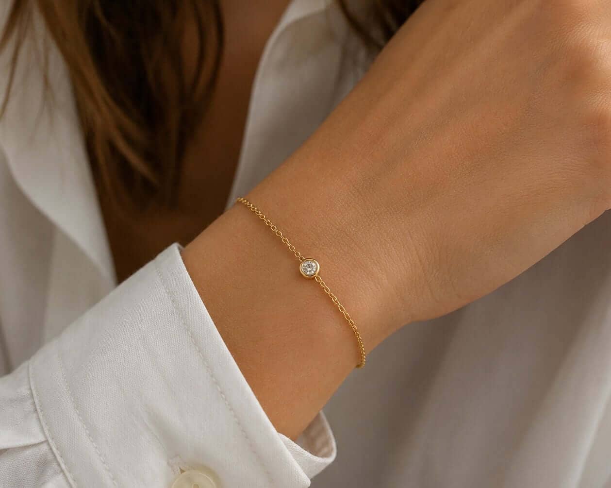 Delicate yellow-gold bracelet with one bezel-set natural diamond worn beside a white shirt cuff
