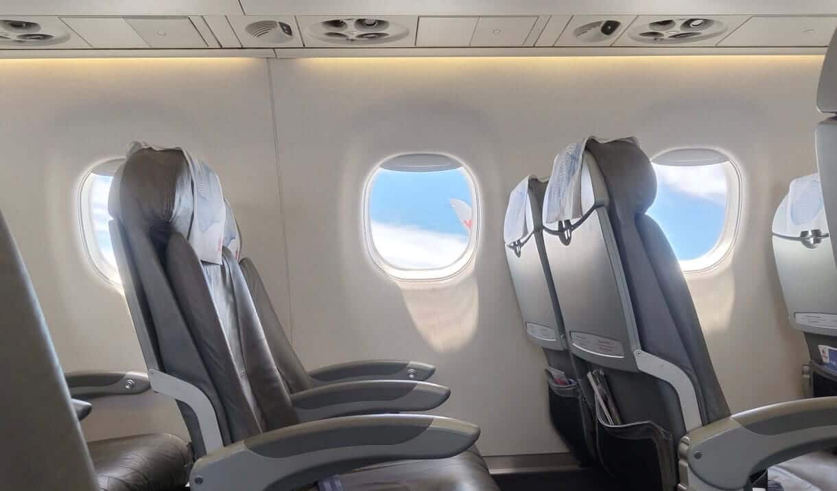 飛機內部空座位與窗外藍天，用以說明大容量背包算隨身行李時，必須符合放入頭頂置物箱的尺寸規範。