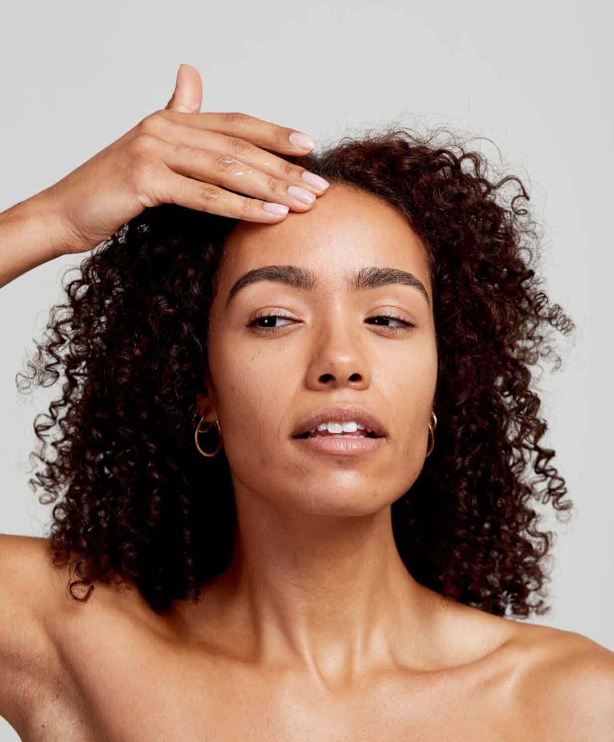 Woman with curly hair touching her face showing healthy glowing skin for winter skincare routine