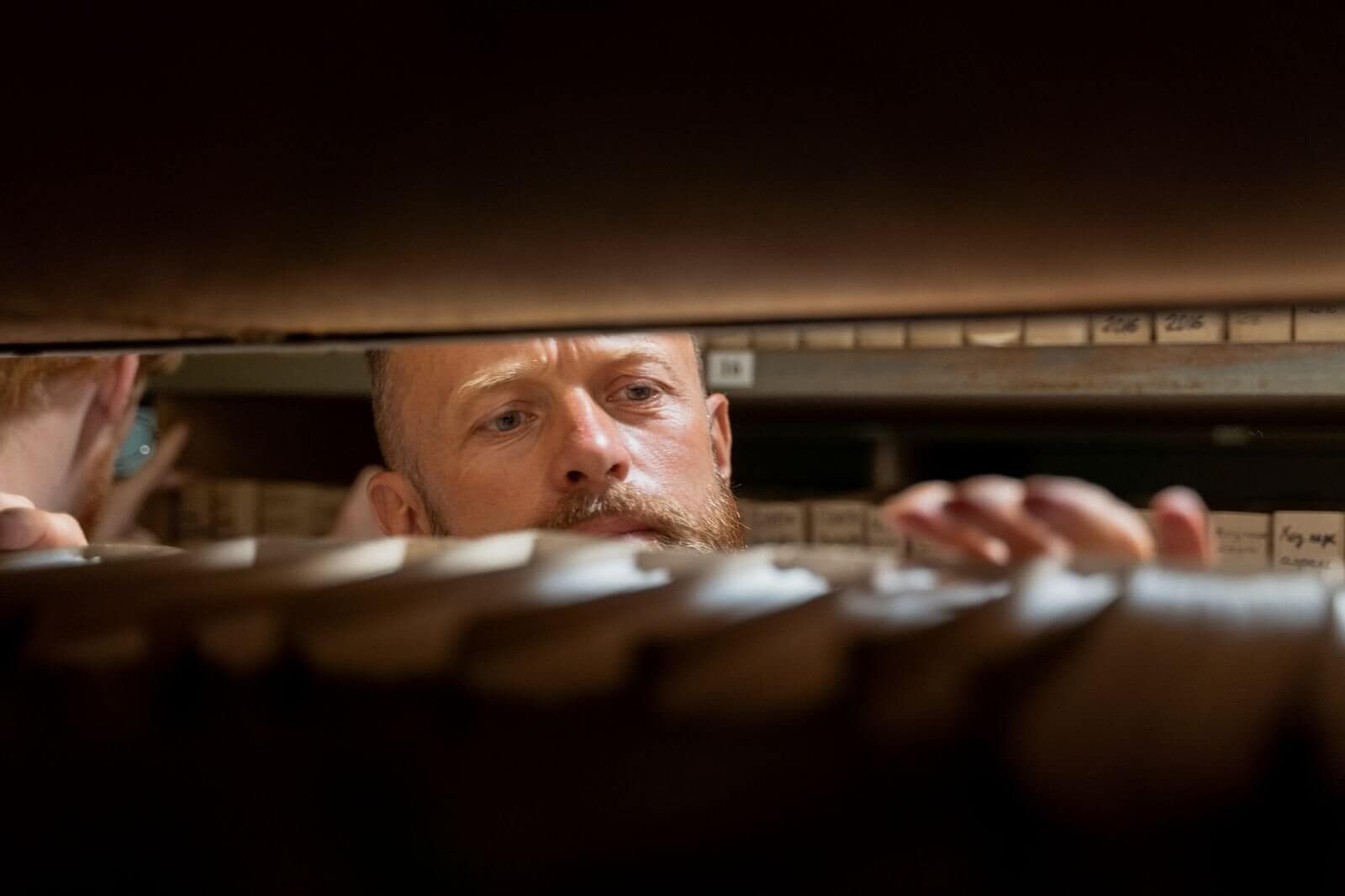 Records staff member searching through a long shelf of stored files, representing the intake and deadline tracking work Colorado body camera records law requires of records units