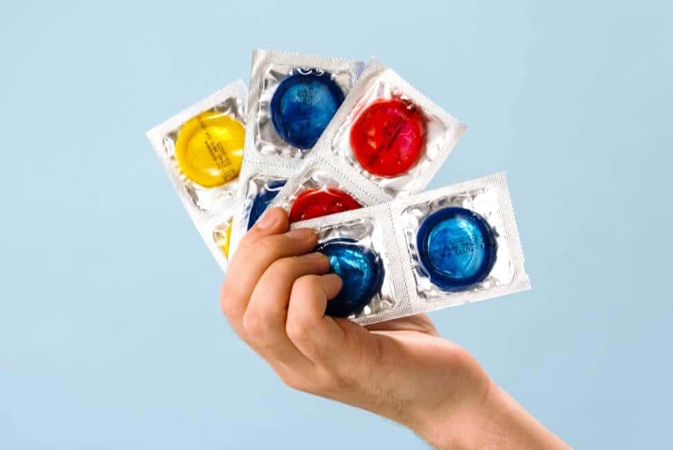 Multiple condoms in different colors held by one hand.