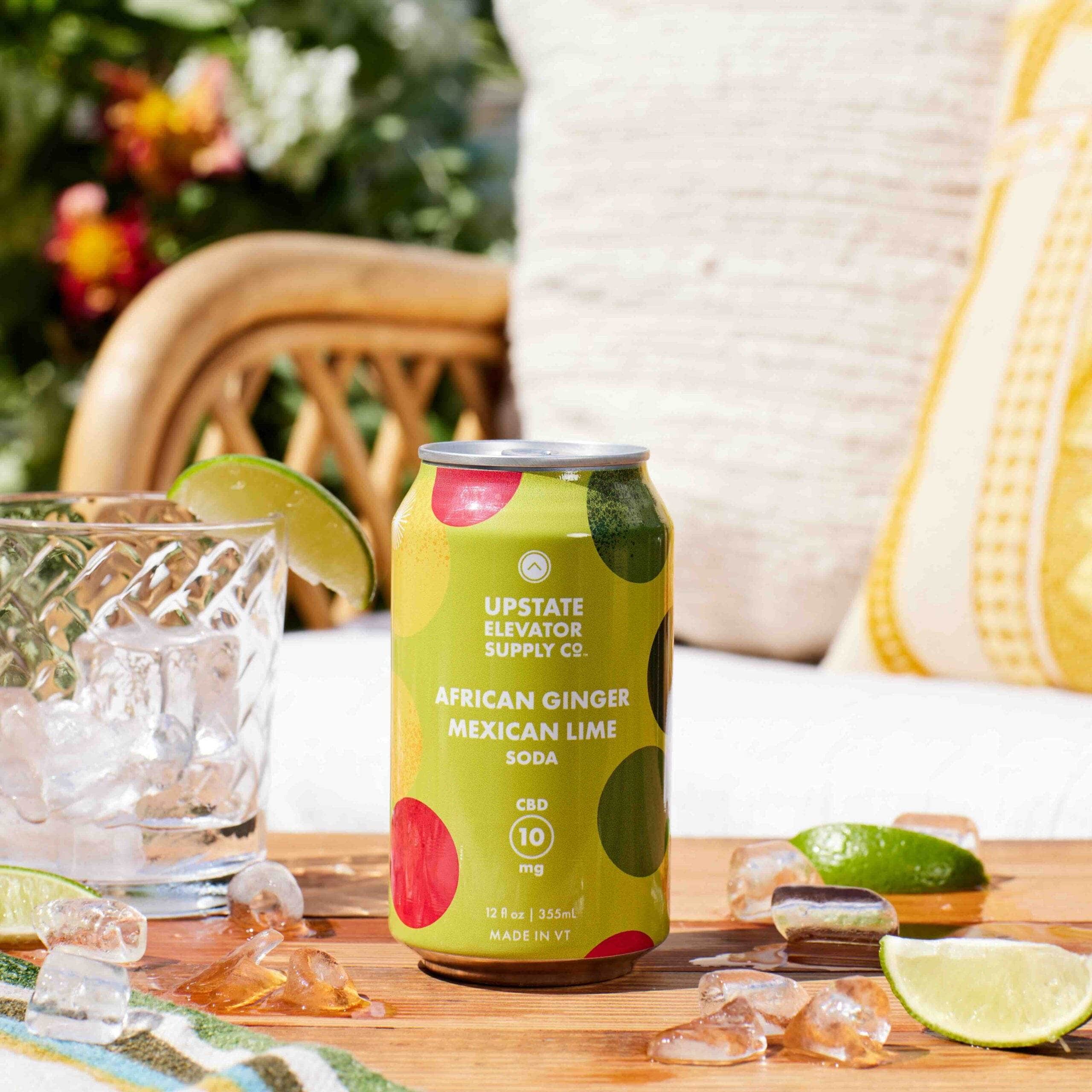 Upstate Elevator African Ginger and Mexican Lime CBD soda can on an outdoor table beside a glass of ice and lime slices