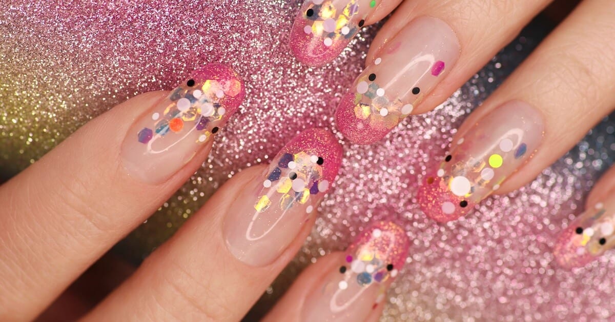 A close-up of someone with colorful glitter nails. The glitter and sequins are placed at the top of the French tip.
