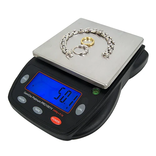 Image of the GEMORO Professional Scale Pro 1001V from Gesswein with a platinum bracelet, platinum ring and yellow gold ring on top. Tghe scale is on. white background.