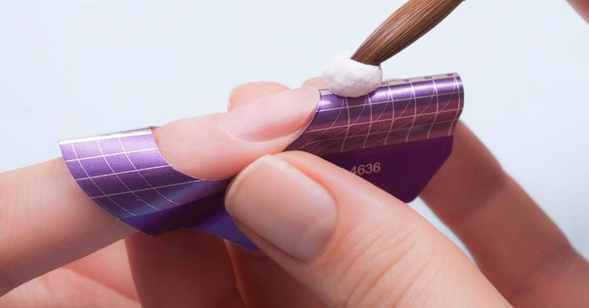 A nail technician placing a bead of acrylic onto a nail form to achieve a longer nail for their manicure client.