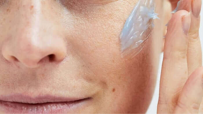 Close-up of woman applying clear skincare serum to her cheek, showing gentle application technique for sensitive skin care