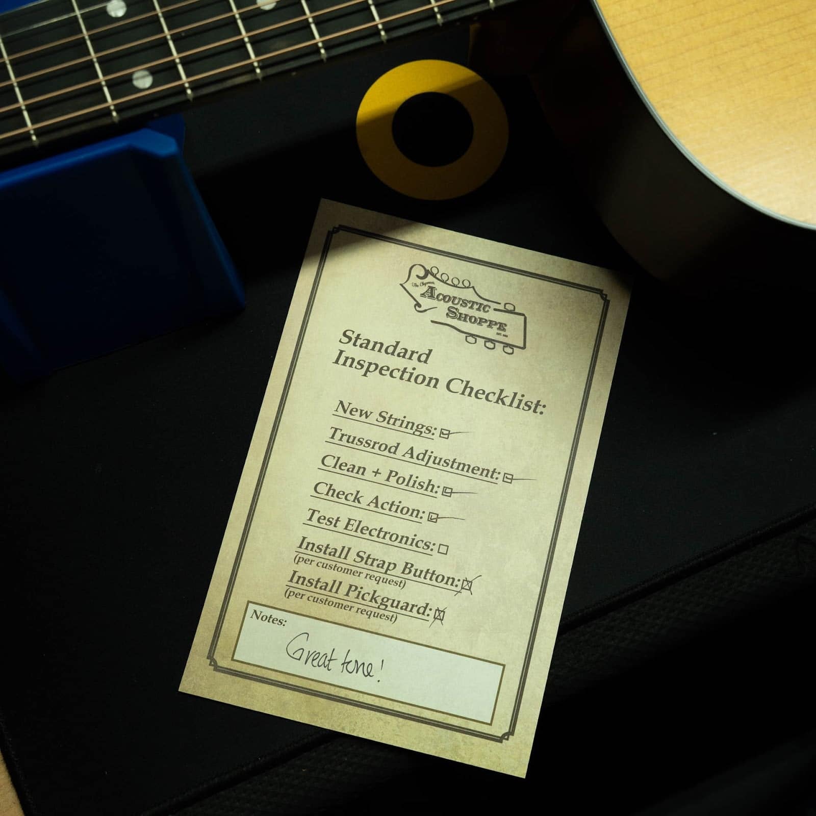 Completed TAS inspection checklist card on the bench beside an acoustic guitar