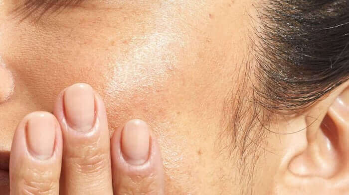 Close-up of fingers gently touching dewy, hydrated skin on forehead showing healthy natural glow