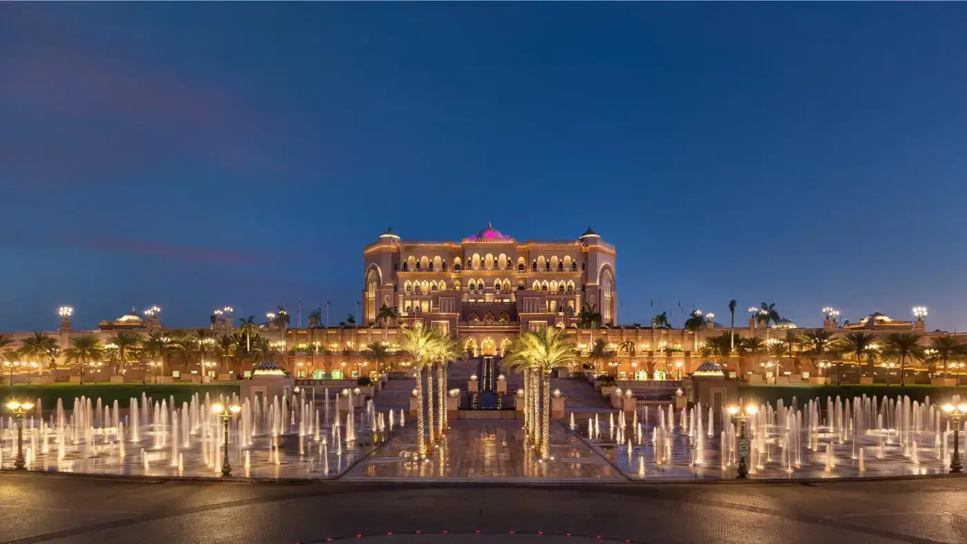 A breathtaking view of a luxurious palace hotel, adorned with intricate details and shimmering lights, reflecting in the waters of a grand fountain.